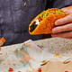Hand holding the Toasted Cheddar Chalupa with black beans, adding mild hot sauce